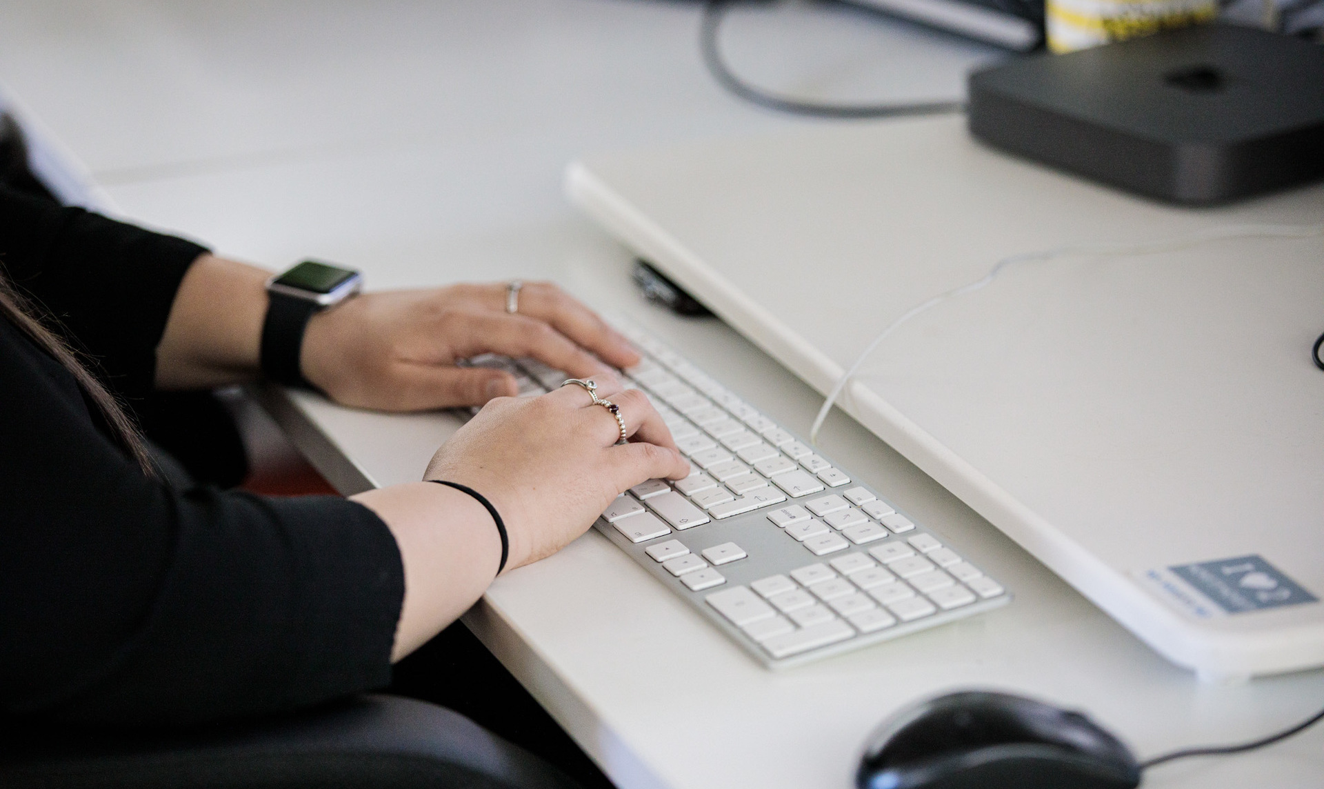 Woman's hands typing on a keyboard sat at a desk.