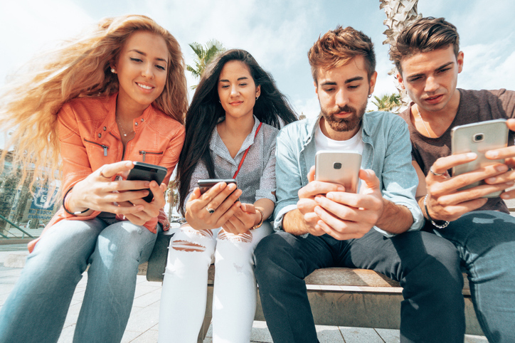 4 teenagers sat down scrolling social media on their mobile.